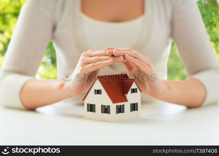 security and home insurance concept - close up of woman protecting house model by hands over green natural background. close up of woman protecting house model by hands