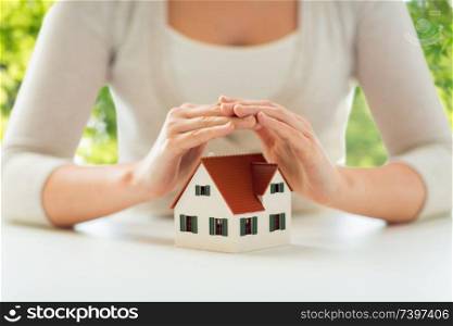 security and home insurance concept - close up of woman protecting house model by hands over green natural background. close up of woman protecting house model by hands