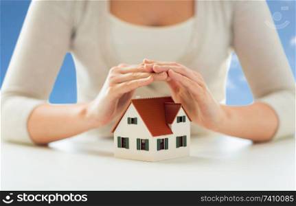 security and home insurance concept - close up of woman protecting house model by hands over blue sky and clouds background. close up of woman protecting house model by hands