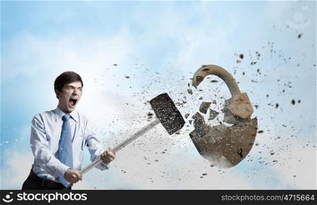 Security concept. Young angry businessman crashing stone lock with hammer