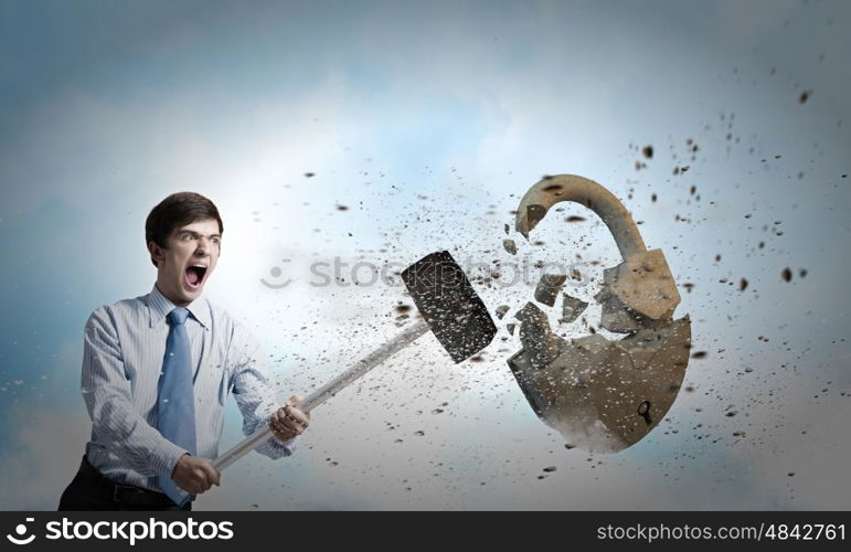 Security concept. Young angry businessman crashing stone lock with hammer