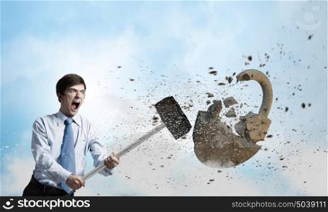Security concept. Young angry businessman crashing stone lock with hammer