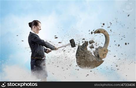 Security concept. Young angry businesswoman crashing stone lock with hammer
