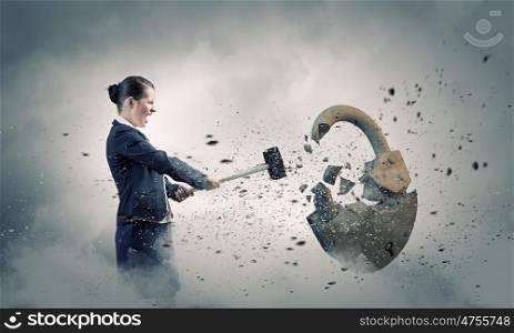 Security concept. Young angry businesswoman crashing stone lock with hammer