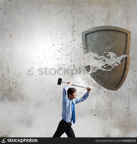 Security concept. Young businessman crashing stone shield with hammer