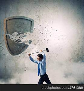 Security concept. Young businessman crashing stone shield with hammer