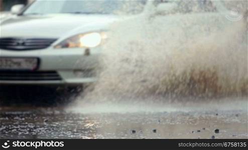 sedan plows through a large puddle on a flooded street making splash