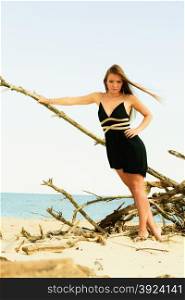 Seductive woman outdoor in summer. Sexual young model in black dress on beach.