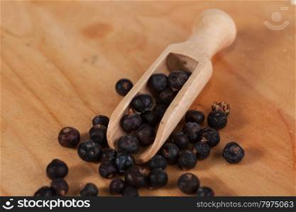 Seeds of juniper with a small wooden spoon. . Seeds of juniper with a small wooden spoon on a wooden tray. Beautiful photos of culinary magazines