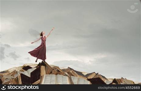 Seek for education and knowledge. Woman in long dress standing on pile of old books