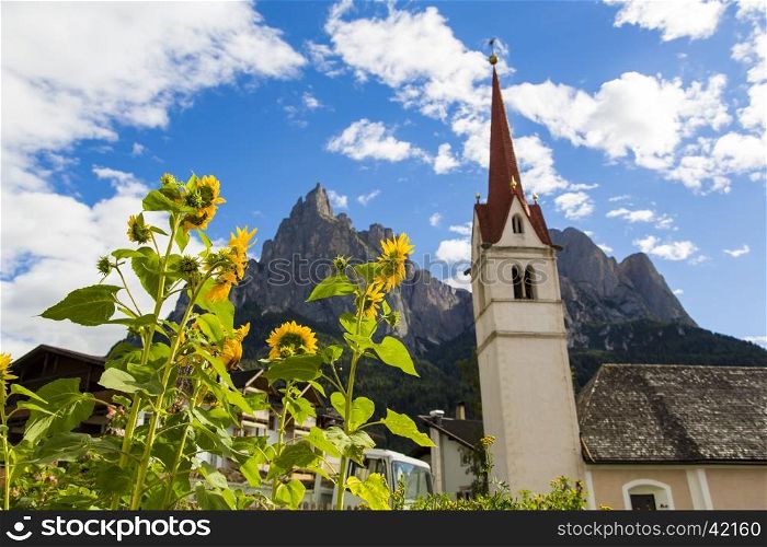 Seiser Alm Schlern, IT- September 19. Botton view of the St. Mary's Assumption with sunflowers in the foreground and Seiser Alm on the background