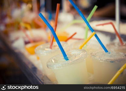Selection of plastic cups with grapefruit juice and colored straws.