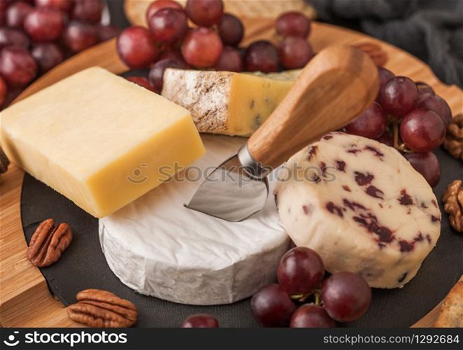 Selection of various cheese on the board and grapes on wooden background. Blue Stilton, Red Leicester and Brie Cheese and nuts.