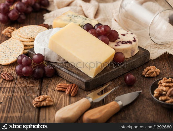 Selection of various cheese on the board and grapes on wooden table background. Blue Stilton, Red Leicester and Brie Cheese with knife and fork.