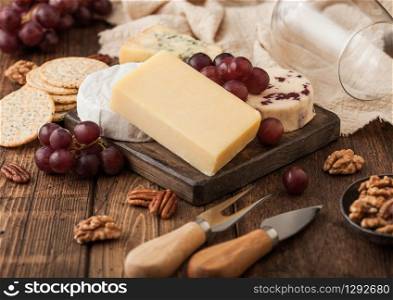 Selection of various cheese on the board and grapes on wooden table background. Blue Stilton, Red Leicester and Brie Cheese with knife and fork.