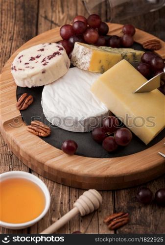 Selection of various cheese on the board and grapes on wooden table background. Blue Stilton, Red Leicester and Brie Cheese with knife on round chopping board.