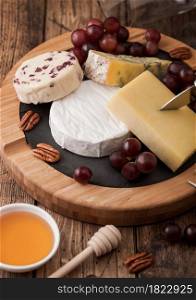 Selection of various cheese on the board and grapes on wooden table background. Blue Stilton, Red Leicester and Brie Cheese with knife on round chopping board.