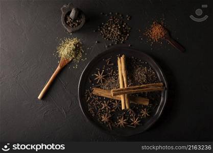 Selection of various spices on textured black background. Pepper, cardamom, clove, cinnamon, star anis, dehydrated parsley.Flat lay