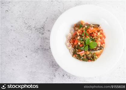 Selective focus appetizers with sardine in tomato sauce and spicy mixed with herb in white plate, blurred spoon and fork, copy space