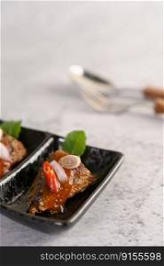 Selective focus appetizers with the spicy sardine in ceramic tray, spoon and fork in blurred background, copy space