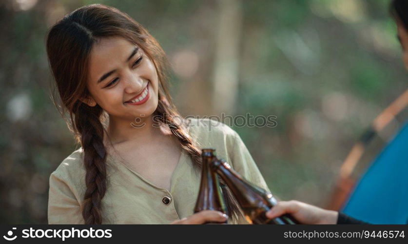 Selective focus, Beautiful Asian woman and friends travelers  relaxing at front of c&ing tent, They enjoy to talking and drinking beer with fun and happy together