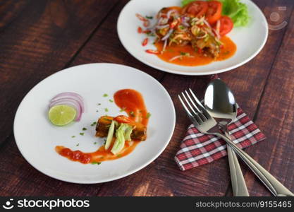 Selective focus canned sardine with tomato sauce and cooking ingredient was beautiful arrangement in white plate, stainless spoon and fork on napkin nearly on wooden table, blurred mixed sardine salad