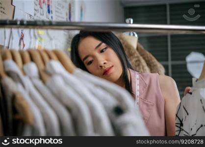 Selective focus, Close up young designer female smile and proud with her clothes design on hanger, tape measure on neck, clothes sketch on board behide her
