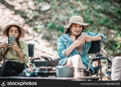 Selective focus, Group of girl friends sitting on c&ing chair and use their smartphone ignoring each other while c&ing in park