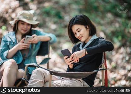 Selective focus, Group of girl friends sitting on camping chair and use their smartphone ignoring each other while camping in park