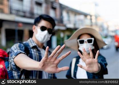 selective focus hands of young backpacker couple in protection face mask and sunglasses keep distance raise palms express negative attitude coronavirus don’t close contact while travel in city street