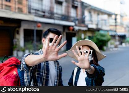 selective focus hands of young backpacker couple in protection face mask and sunglasses keep distance raise palms express negative attitude coronavirus don&rsquo;t close contact while travel in city street