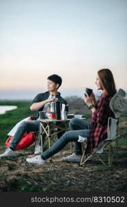 Selective focus, handsome man making fresh coffee grinder, Cheerful Young backpacker couple sitting at front of the tent near lake with coffee set while c&ing trip on summer 