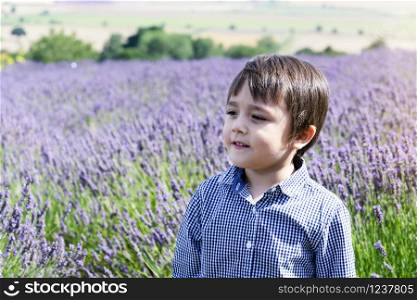 Selective focus little boy with smiling face standing in lavenders field, Portrait of happy kid playing outdoors with blurry flowers background, Child having fun in lavender garden in the summer.