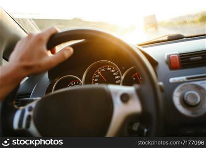 Selective focus man&rsquo;s hand on steering wheel, driving a car at sunset. Travel background.. Selective focus man&rsquo;s hand on steering wheel, driving a car at sunset. Travel background