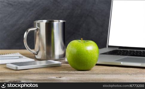 Selective focus of a fresh green apple on school desk with technology. Layout in horizontal format with copy space.