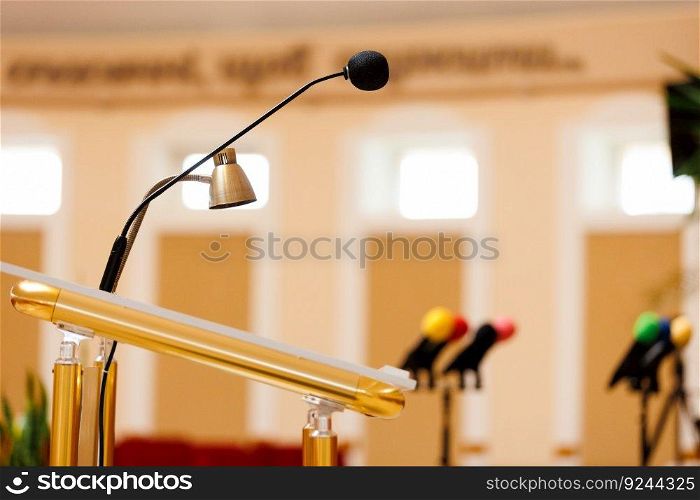 Selective focus of a microphone with other colorful microphones on podium blurred in the background. Concept of communication, media, press conference, event, performance, politics, company. Selective focus of a microphone with other colorful microphones on podium blurred in the background. Concept of communication, media, press conference, event, performance, politics, company.