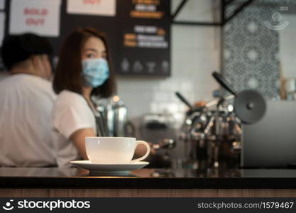 Selective focus of coffee cup and background of Asian barista woman wearing face masks To prevent contagious diseases And brewing coffee in the coffee shop. The concept of prevention from COVID 19