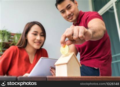 Selective focus of golden coin. Happy Asian couples smiling Because it is profitable from investment And have savings for buying a home and accommodation. Investment concepts and financial planning