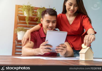 Selective focus of golden coin. Happy Asian couples smiling Because it is profitable from investment And have savings for buying a home and accommodation. Investment concepts and financial planning