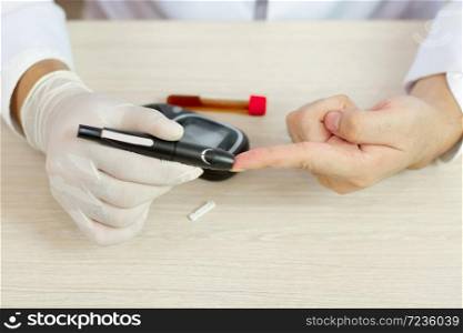 Selective focus of hands using lancet on finger to check blood sugar level by Glucose meter on chart background.