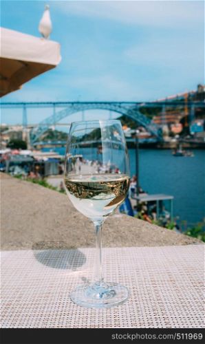 Selective focus of white wine glass overlooking Cais da Ribeira and Ponte de Dom Luis I on the River Douro in Porto, Portugal - reflection of bridge on glass. White wine glass overlooking Cais da Ribeira on the River Douro in Porto, Portugal