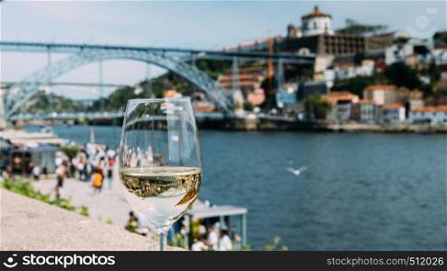 Selective focus of white wine glass overlooking Cais da Ribeira and Ponte de Dom Luis I on the River Douro in Porto, Portugal - reflection of bridge on glass. White wine glass overlooking Cais da Ribeira on the River Douro in Porto, Portugal
