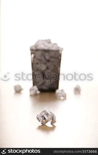 Selective focus of wire mesh trash can with crumpled paper scattered around.