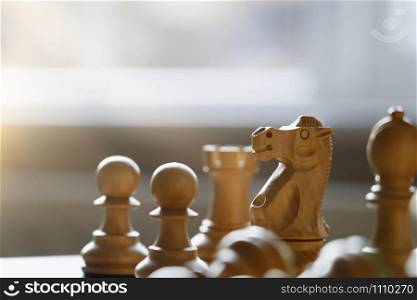 Selective focus of wood knight chess on board game with blurry window background, Business leader and confrontation solve problems concept, Soft focus of Chess horse on board with copy space