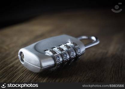Selective focus on 4 digits code number of silver combination pad lock on wooden table, dark tone dim light background. Data protection, key management, password access, security encryption concepts.
