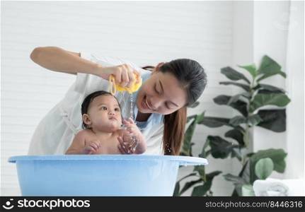 Selective focus on Asian young mother hand holding sponge and squeeze water to drop on her little baby hand while mom bathing cute daughter in bathtub at home, Baby bathing concept. White background