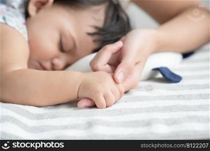 Selective focus on baby hand. Adorable mixed race, Caucasian and Asian, little baby girl is sleeping and holding mother"s finger in her hand at bedroom at home. Purity and innocence concept