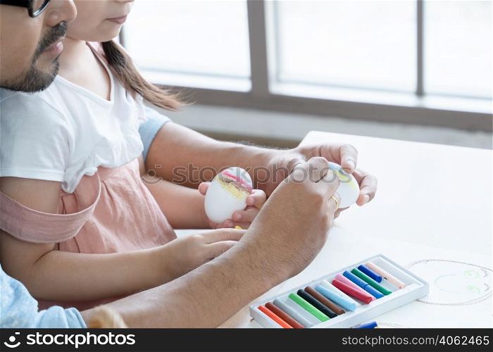 Selective focus on bearded father?s hands teaching little girl daughter decorate Easter egg with colorful crayon at home. Happy family prepare for Easter holiday together