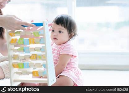 Selective focus on Caucasian cute 7 months daughter toddler baby face looking and playing with alphabet blocks toy, sitting on floor with mother at home. Development, education, growth child care