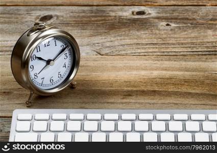 Selective focus on desktop retro metal clock with partial keyboard in foreground. Layout in horizontal format on rustic wood.